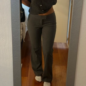 Grå kostymbyxor med bootcut - Säljer ett par stilrena grå kostymbyxor med bootcut-snitt och låg midja. Byxorna har en klassisk look med dold knäppning framtill och är perfekta för dig som gillar en clean och dressad stil. Materialet är väldigt mjukt, endast använda 1 gång men blivit lite nopprande
