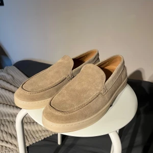 Beige mockaloafers från Mango - Snygga loafers i beige mocka från Zalando med platt, ljus sula och klassisk rund tå. Skorna har en stilren och enkel design som passar perfekt till jeans eller chinos. Mjukt material och bekväm passform för en avslappnad men ändå uppklädd look. Har aldrig använt dem för att de var för stora.