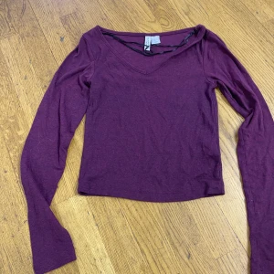 Vinröd långärmad topp från Divided - Vinröd långärmad topp från Divided med v-ringning och smal passform. Tillverkad i mjuk bomullsmix och har en enkel, stilren look. Perfekt att matcha med jeans eller kjol för en chill vibe.