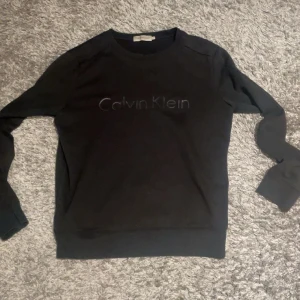 Svart Calvin Klein sweatshirt - Svart sweatshirt från Calvin Klein med diskret logga framtill. Klassisk rund halsringning och långa ärmar. Mjuk och skön bomullsblandning, perfekt för en chill och stilren look.
