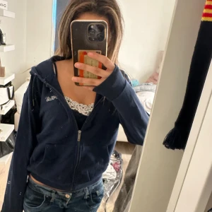 Mörkblå zip-hoodie från Fila - Säljer en mörkblå hoodie från Fila med dragkedja framtill och huva. Tröjan har långa ärmar, två fickor och en broderad Fila-logga på bröstet. Perfekt för en chill och sportig look.