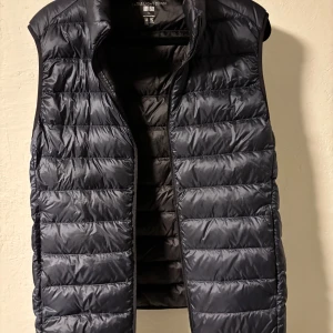 Marinblå dunväst från Uniqlo, S - Säljer en, quiltad dunväst från Uniqlo Ultra Light Down. Västen är lätt, har vattenavvisande yta och stängs med dragkedja. Perfekt att slänga över en hoodie eller tröja när det är kyligt ute. Klassisk och stilren design.