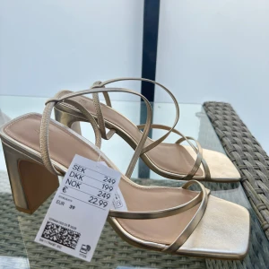 Guldiga sandaler med klack och remmar - Snygga sandaler i guld med tunna remmar och fyrkantig tå. Skorna har en hög klack och öppen tå. Helt nya ifrån H&M  men har inte hittat tillfälle att använda dom så nu söker dom nytt hem :) 