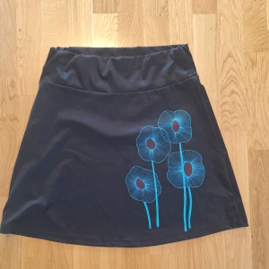 Svart kortkjol med blå blommor Misslook - Svart kortkjol från Misslook med snyggt blått blommönster på ena sidan. Kjolen har en enkel, lätt utsvängd form och bred midjeresår för skön passform. Materialet känns mjukt och stretchigt, perfekt för en chill och trendig look.