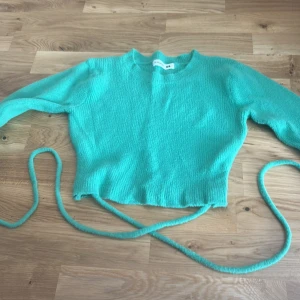 Turkos stickad tröja från Terranova - Mysig turkos stickad tröja från Terranova i storlek XS. Tröjan har långa ärmar, rund halsringning och en croppad passform med snörning i midjan som ger en trendig look. Perfekt för att lyfta din outfit med lite färg.