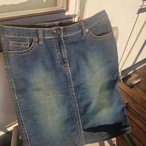 Klassisk blå jeanskjol med fickor - Snygg blå jeanskjol med klassisk femficksdesign och kontrastsömmar. Kjolen har bälteshällor, knapp och dragkedja framtill samt bakfickor med dekorativa sömmar. Perfekt för dig som gillar en tidlös och avslappnad stil.