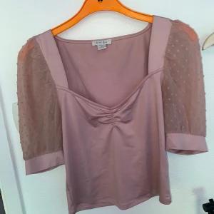 Rosa blus med meshärmar från Amisu - Supersöt ljusrosa blus från Amisu med transparenta meshärmar som har små prickar. Blusen har v-ringning och lätt rynk framtill. Perfekt för dig som gillar romantiska detaljer och en feminin look.