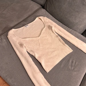 Beige ribbad topp från Bubbleroom - Säljer en beige ribbad långärmad topp från Bubbleroom. Toppen har en snygg v-ringning och figurnära passform som framhäver siluetten. Materialet är mjukt och stretchigt, perfekt för en trendig och stilren look.