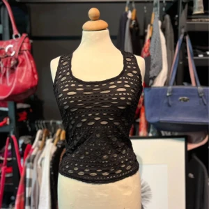 Svart hålmönstrad topp från Bik Bok - Svart ärmlös topp från Bik Bok med hålmönster och transparent tyg under. Toppen är figurnära och tillverkad i 100% polyester. Rundad halsringning och stretchigt material.