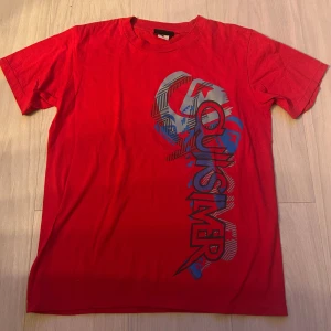 Röd Quiksilver t-shirt med tryck - Snygg röd t-shirt från Quiksilver med stort grafiskt tryck. Helt ny.. Storlek M. Klassisk rund hals och korta ärmar. Perfekt för dig som gillar streetwear och vill sticka ut lite extra. Materialet är mjuk bomull.
