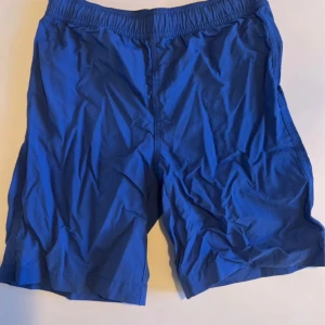 Blå badshorts från Mywear Young - Snygga blå badshorts från Mywear Young med elastisk midja och innerbyxa i mesh. Shortsen har en bakficka och är perfekta för sommardagar vid stranden eller poolen. Klassisk modell med relaxed fit och enkel design.