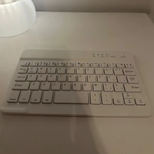 Trådlöst Bluetooth-tangentbord - Kompakt och stilrent vitt Bluetooth-tangentbord i gott skick. Perfekt för surfplattor, laptops eller smartphones. Lätt och portabel design, med tydliga knappar och indikatorlampor för laddning och anslutning. Inga synliga repor eller skador. Passar perfekt in i iPad mini och har magnetisk baksida så att den fastnar i skal!