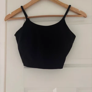 Svart linnetopp från Relode - Säljer en svart croppad linnetopp från Relode med tunna axelband och stilren design. Toppen har en enkel, tight passform och är perfekt för träning eller som ett snyggt basplagg. Relode-logga i vitt på sidan ger en sportig touch.