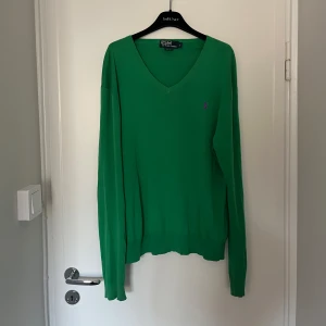 Grön v-ringad tröja Polo Ralph Lauren - Grön v-ringad tröja från Polo Ralph Lauren i slim fit-modell. Tröjan har långa ärmar och en liten lila broderad logga på bröstet.