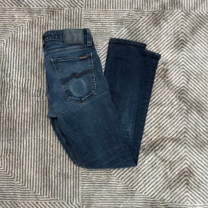Mörkblå jeans från Nudie Jeans - Snygga mörkblå skinny jeans från Nudie Jeans med klassisk femficksdesign och diskret broderad bakficka. Jeansen har smal passform och är tillverkade i stretchig denim för extra komfort. Perfekta för dig som gillar en stilren look.