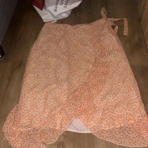 Omlottkjol med volang från Vero Moda - Superfin omlottkjol från Vero Moda  med orange leopardmönster. Kjolen har volangkant 
