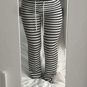 Randiga svarta och vita mjukisbyxor - Säljer ett par svarta och vita mjukisbyxor med horisontella ränder och snörning i midjan. Byxorna har en skön loose passform och är tillverkade i ett ribbat, stretchigt material. Low waist och flare/bootcut!!