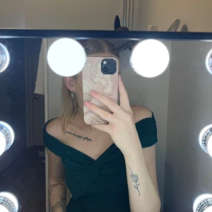 Mörkgrön offshoulder topp - Säljer en mörkgrön offshoulder topp med snygg twistad detalj framtill. Den har en tight passform och är tillverkad i ett mjukt, stretchigt material. Perfekt för dig som vill sticka ut med en elegant och modern look.