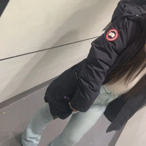 Canada goose  - Säljer en svart Canada Goose dunjacka med huva och klassisk logga på ärmen. Jackan har flera fickor framtill, dragkedja och knappar, samt ribbade muddar vid ärmsluten. Perfekt för kalla dagar och riktigt snygg streetstil. Den är lite sliten, som ni ser på dom två sista bilderna. Billigare pris vid snabb affär!!
