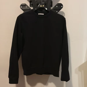 Svart sweatshirt från Zara - En stilren svart sweatshirt från Zara med rund hals och långa ärmar. Tröjan har en klassisk passform och är tillverkad i mjukt material som känns skönt mot huden. Perfekt för dig som gillar enkel och clean stil.