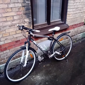 Scott Aspect 15 - Bilderna visar en cykel av märket Scott, modell Aspect 15 Com. Cykeln har en svart ram med vita detaljer, skivbromsar, stänkskärmar och flaskhållare. Sadeln är vit och cykeln ser ut att vara i begagnat skick med viss smuts och slitage, men inga synliga större defekter.