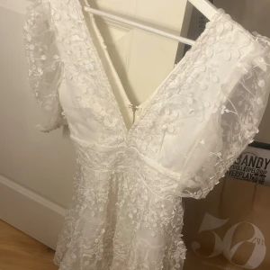 Vit kortklänning från Showpo - Superfin vit kortklänning från Showpo med blommigt broderat mönster och transparenta, korta ärmar. Klänningen har v-ringning och dragkedja i ryggen. Endast använt en gång. Perfekt till studenten!! Skriv gärna innan ni trycker på köp💞