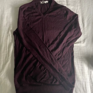 Vinröd v-ringad stickad tröja - Snygg vinröd stickad tröja med v-ringning och långa ärmar. Perfekt för dig som gillar stilrena och enkla plagg med lite djupare färg. Mjuk och skön känsla, passar till jeans eller chinos. Ribbad kant vid ärmslut och nederkant.