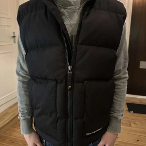 Svart vintage dunväst från Peak Performance - Svart dunväst från Peak Performance med hög krage och två stora fickor framtill. Pris kan diskuteras