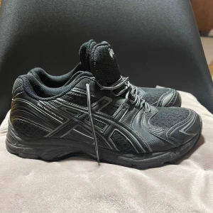 Svarta Asics Igs sneakers - Svarta Asics Gel-Tech Walker sneakers med sportig design, meshpaneler för andning och detaljer i syntet. Skorna har snörning och en robust, bekväm sula som passar perfekt för långa promenader eller träning. Klassisk Asics-logga på sidan och plös.