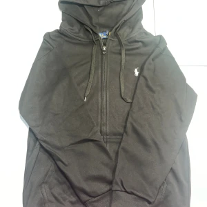 Ralph lauren hoodie - Svart hoodie från Polo Ralph Lauren med dragkedja och huva. Klassisk broderad logga i vitt på bröstet och snörning vid huvan. Tröjan har ribbade muddar och är tillverkad i mjuk bomull, perfekt för chill stunder. Hör av dig vid minsta fundering!