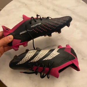 Adidas Predator freak fotbollsskor svart/rosa - Säljer ett par Adidas Predator fotbollsskor i svart och rosa med vita detaljer. Skorna har snörning, låg profil och mönstrad ovansida för extra grepp. Snygg design med stickad material runt ankeln och robust plastsula med dobbar för gräsplan. Dem är matchklara, lätta och bekväma. Priset kan diskuteras!