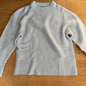 Ljusgrå stickad tröja  - Mysig ljusgrå stickad tröja med rund halsringning och ribbade muddar. Perfekt för lager-på-lager och chill dagar. Enkel och stilren design som passar till det mesta.