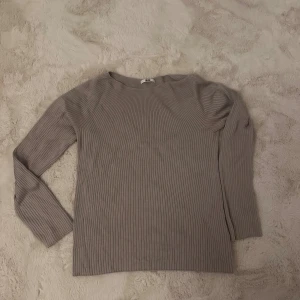 Ribbad tröja från Uniqlo - Ribbad långärmad tröja från Uniqlo med rund halsringning. Färgen är svår att lista ur den är nog mer beige men åt det mer lila hållet. Tröjan har en enkel och stilren design. Materialet är stretchigt för en bekväm passform.