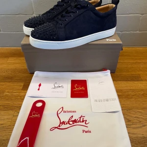 Christian Louboutin - Exklusiva mörkblåa sneakers från Christian Louboutin i mocka med svarta nitar på tån och klassisk röd sula. Skorna har snörning, rund tå och vit platt sula. Kommer med originalkartong, dustbag och tillbehör. Perfekt för dig som vill sticka ut med lyxig streetstyle. Kvitto finns också. Strl 45 men sitter som 44. Säljer då jag andände dem lite men dem var för små