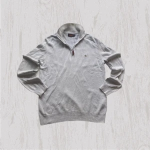 Ljusgrå half zip tröja från Morris - Snygg ljusgrå tröja från Morris i 100% bomull. Half zip-dragkedja vid kragen och diskret broderad logga på bröstet. Långärmad med ribbade muddar och förstärkta armbågar. Perfekt för dig som gillar stilrena och klassiska plagg.