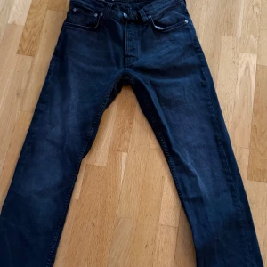 Svarta jeans från Nudie Jeans, 30/30 - Snygga svarta jeans från Nudie Jeans i klassisk femficksmodell. Jeansen har raka ben, normal passform och är tillverkade i slitstark bomull. Perfekt för dig som gillar stilrena och tidlösa jeans med diskreta detaljer på bakfickorna.