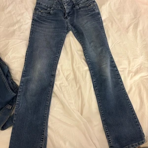 Blå bootcut jeans från Monali - Snygga blå jeans från Monali med klassisk bootcut passform och fem fickor. Jeansen har en låg midja, slitningar och detaljerade sömmar på bakfickorna. De har ett midjemått på ca 38 cm och innerbenslängd är ca 78❣️ hör av er vid intresse, dessa är aldrig använda! 