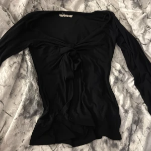 Svart långärmad topp med knyt - Svart långärmad topp från Design by Si i storlek XS/S. Toppen har en snygg v-ringning och ett knyt framtill som ger en cool och feminin touch. Mjuk och följsam passform, perfekt att styla med jeans eller kjol. Materialet känns lätt och skönt mot huden. Säljer för två hundra men pris kan diskuterats 