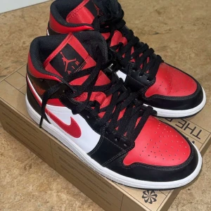 Nike Air Jordan 1 High röd/svart - Säljer ett par Nike Air Jordan 1 High sneakers i klassisk röd, svart och vit färg. Skorna har snörning, rund tå och platt sula. Ikonisk design med läderpaneler och den röda swoosh-loggan på sidan. Perfekta för dig som gillar streetwear och sneakers med attityd.
