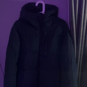 Mörkblå vinter jacka Mckinley - Säljer en mörkblå pufferjacka med huva och dragkedja framtill. Jackan har en clean look med diskreta sömmar och en bröstficka med dragkedja. Perfekt för kalla dagar när du vill hålla värmen och ändå se stilren ut. Nypris 900kr