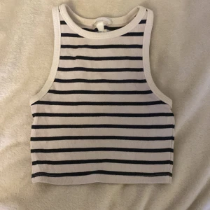 Randig croppad linnetopp  - Säljer en croppad linnetopp med svarta och vita horisontella ränder. Toppen är ärmlös med rund halsringning. Tillverkad i ribbad bomull för en skön och stretchig känsla. Perfekt för en chill och stilren look, nästan aldrig använt💕