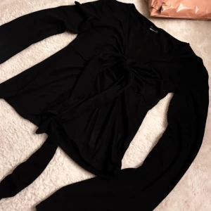 Svart omlottopp med knyt från Gina Tricot - Svart långärmad omlottopp från Gina Tricot i storlek XS. Toppen har snygg knytning framtill och lätt v-ringad hals. Materialet är mjukt och stretchigt, perfekt för en trendig look. Ärmarna är långa och toppen har en slim passform. Har tyvärr blivit för liten💕