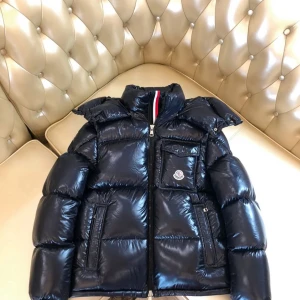 Svart pufferjacka från Moncler - Snygg svart pufferjacka från Moncler med glansig finish, hög krage och dragkedja framtill. Jackan har en bröstficka med Moncler-logga, två sidofickor och quiltad design. Perfekt för kalla dagar och ger en cool streetstyle-vibe.