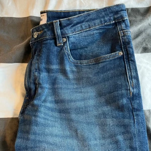 Blå raka jeansbyxor  - Klassiska blå jeansbyxor från Wear med raka ben och normal passform. Jeansen har fem fickor, bälteshällor och snygga slitningar för en avslappnad look. Perfekta till sneakers eller boots och funkar året runt.