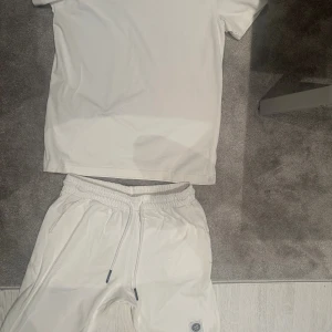 Vit Stone Island set - Helt ny vit t-shirt från Stone Island i storlek S. Klassisk design med korta ärmar och rund hals. T-shirten har den ikoniska Stone Island-loggan på vänster ärm och är gjord i mjuk bomull. Perfekt för dig som gillar stilrena och exklusiva plagg. Samt ett par vita shorts i storlek M perfekt och stillrent.