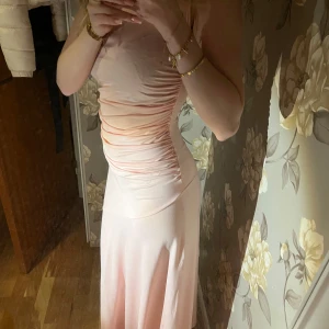 Ljusrosa långklänning från SHEIN - Supersnygg ljusrosa långklänning från SHEIN i storlek S. Klänningen har figurnära passform med rynkade detaljer längs sidorna och är ärmlös med smala axelband. Materialet är mjukt och stretchigt, troligtvis polyester, vilket ger en skön känsla och fin lyster.