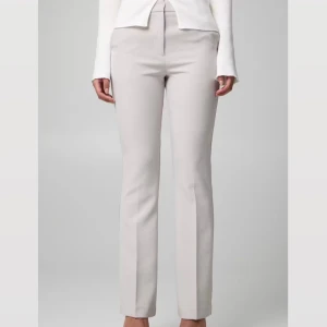 Ljusbeige kostymbyxor med raka ben - Snygga ljusbeige kostymbyxor med raka ben och pressveck.. Materialet känns mjukt och har en lätt stretch. Kostymbyxorna är helt oanvända, prislappen ligger kvar.