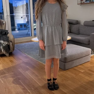 Ljusgrå kortklänning med volang - Säljer en ljusblå kortklänning med diskret prickigt mönster och volanger på axlarna, säljer pga för liten på bilden är jag 155 