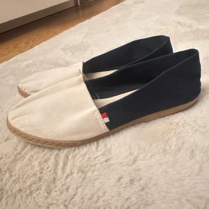 Tommy Hilfiger espadrillos skor - Snygga espadrillos från Tommy Hilfiger i marinblått och vitt tyg med naturfärgad flätad sula. Skorna har en klassisk, spetsig tå och liten logodetalj på sidan. Perfekta för sommaren och lätta att matcha till olika outfits. Köpt för flera år sedan.