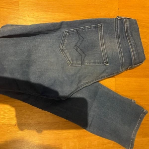 Blå Replay jeans med raka ben - Säljer ett par klassiska blå jeans från Replay med raka ben och snygga detaljer på bakfickan. Jeansen har normal passform och är tillverkade i mjukt jeanstyg med diskret tvätt. Perfekta för dig som gillar stilrena och tidlösa jeans.